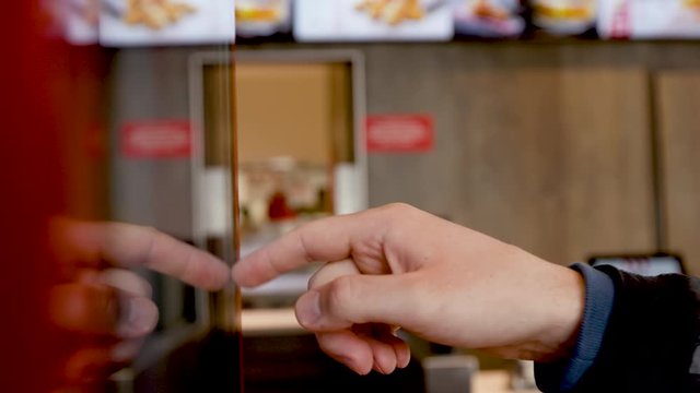 Man uses interactive touchscreen display of electronic multimedia kiosk - scrolling and touching, close up shot. Person swipes screen making an order. Service, education and technology concept.