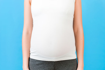 Close up shot of young pregnant woman's belly in home clothing at blue background. Pregnancy concept. Copy space