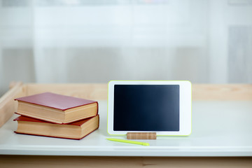 White tablet and books on white table. Home office while self-isolation, working from home. Online education, e-learning while quarantine.