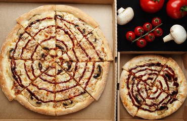 Large and small pizzas lie on an open cardboard box. Next to them are cherry tomatoes and mushroom mushrooms. top view