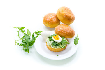 Homemade bun with cheese spread, fresh arugula and boiled egg in a plate