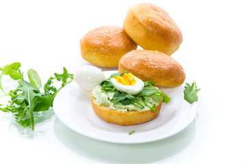 Homemade bun with cheese spread, fresh arugula and boiled egg in a plate