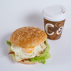 burger with egg and salad on a white background. Nearby is a paper cup with a coffee closeup