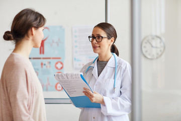 Young female doctor in white coat standing with medical card and prescribing a medicine for her...