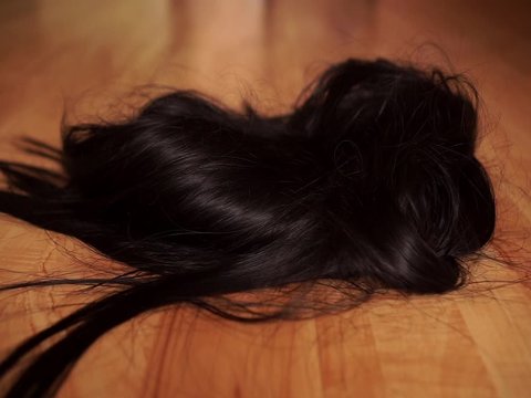A girl in black shoes walks on a wooden floor and drops a black wig on the floor. The concept of dressing up, freaks or party