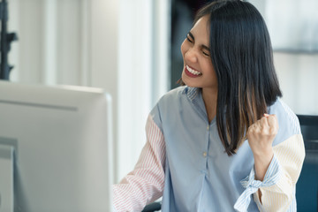 Successful excited working woman raised arm with happy at work in front of computer monitor.
