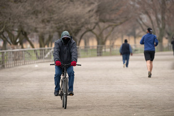 unknown man wearing a mask rides his bike in the park during the Corona Virus