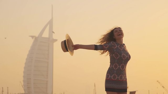 Portrait young happy charming beautiful woman tourist. Girl laughs has fun dancing on coast line Dubai. Hairstyle blond long hair fluttering. Straw beach hat. Backdrop yellow sunny sunset. UAE 2020 4k