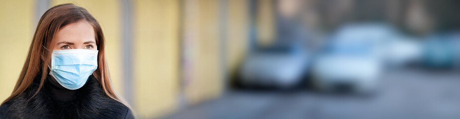 Young woman wearing disposable blue virus face mouth nose mask, closeup portrait, blurred wall and cars background, banner space for text right side. Coronavirus covid-19 outbreak prevention concept