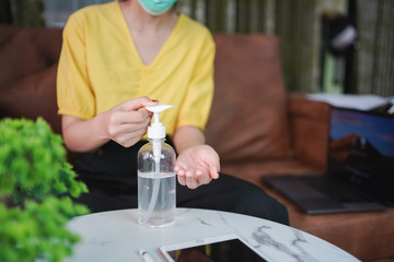 Asian woman sitting on couch and wearing medical mask. Stay at home. Concept prevention COVID-19, Coronavirus outbreak situation, Cleaning her hands with sanitizer gel.