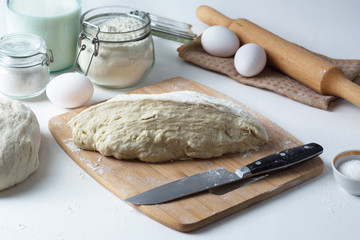 the dough lies on the table, next to a wooden rolling pin, flour and ingredients, pastries