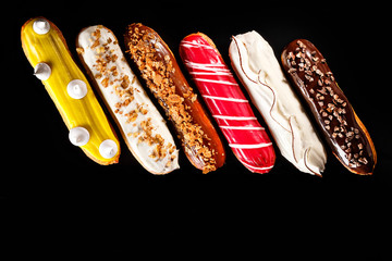 Assorted eclairs with cream filling and elegant decorative toppings for confectionary photography concept in black background.