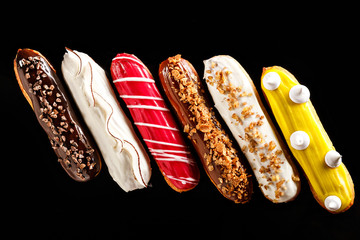 Assorted eclairs with cream filling and elegant decorative toppings for confectionary photography concept in black background. Art desserts