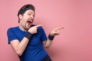 Happy sportsman pointing with finger on pink wall with copyspace