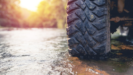 Part of the mud-wheeled off-road opto-trailer parked in a stream with running water. with warm light. © PIPAT