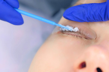 Beautician applying solution for lamination on woman lashes on curlers, lift eyelashes procedure in...