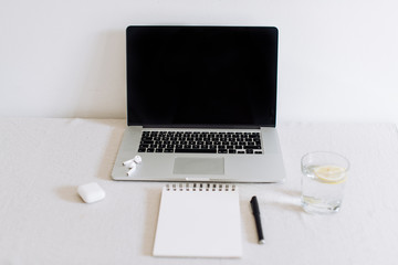 Minimalistic working space at home during Covid-19 pandemic. Opened laptop, notebook, pen, glass of water with lemon and wireless headphones