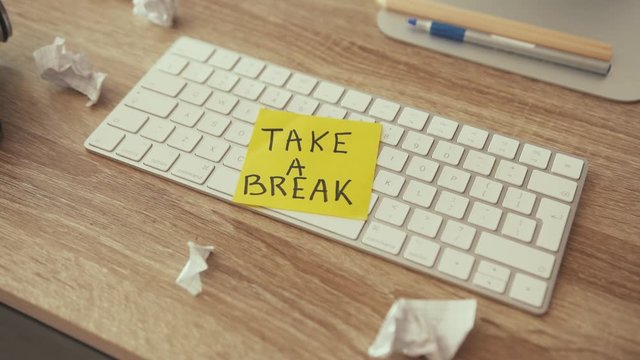 Creative clutter on working office desk. Yellow remark sticker note saying to take a break. Concept of minimalism, motivation. Work from home.