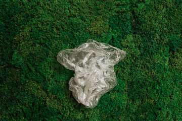 a plastic bag lies on the green grass of moss, place for text, environmental issue, waste recycling, pollution of the planet