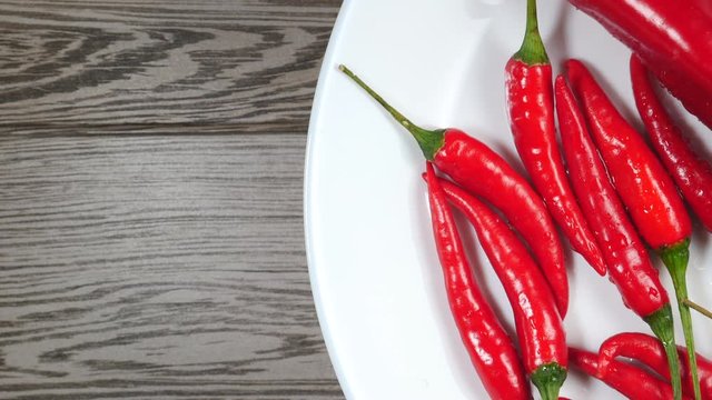 Top View Of Fresh Raw Red Chili Peppers And Ramiro Pepper With Water Drops Rotating On A White Plate On A Gray Wooden Background On The Right Side.