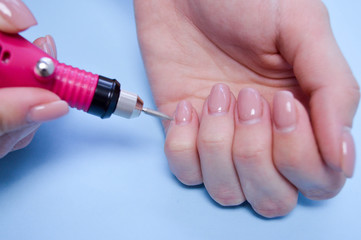 The process of making a beautiful manicure on the fingers of a finger processing a nail with a special machine in a nail beauty salon on a blue background