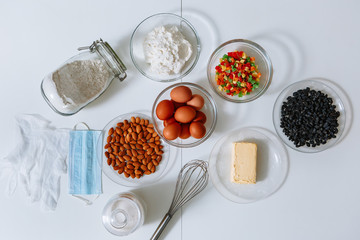 Ingredients for making a cake are on the kitchen table, top view. Medical mask and gloves on the table