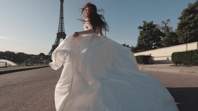 Young bride running in slow motion waving dress and long veil on background of Eiffel Tower. Paris. France