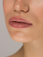 Obraz premium Cosmetics, makeup and trends. Bright lip gloss and lipstick on lips. Closeup of beautiful female mouth with natural lip makeup. Beautiful part of female face. Perfect clean skin in natural light