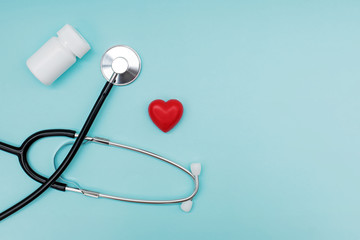 Conceptual photo of a black stethoscope, small heart and bottle of pills on blue background