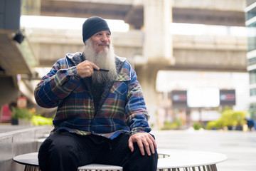 Mature handsome hipster man combing beard in the city streets outdoors