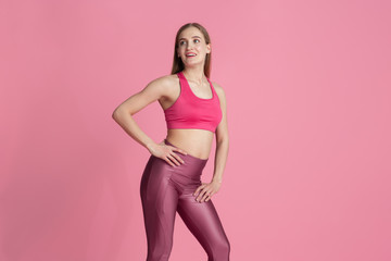 Fototapeta na wymiar Graceful. Beautiful young female athlete practicing in studio, monochrome pink portrait. Sportive fit caucasian model posing. Body building, healthy lifestyle, beauty and action concept.