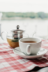 Kettle and cup with fruit tea on the background of the river. Selective focus.