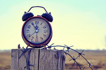 Old retro alarm clock on post tied with barbed wire symbolizes arrival of spring.