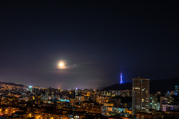 Fototapeta premium Moon rising and stars in night sky over Tbilisi