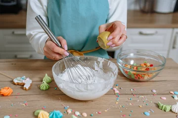 Foto op Canvas The smiling girl cook whips up the icing for the Easter cake with a whisk and squeezes a lemon into it © Alexey Tsibin