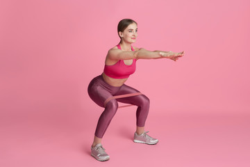 Fototapeta na wymiar Lower body. Beautiful young female athlete practicing in studio, monochrome pink portrait. Sportive fit caucasian model with elastics. Body building, healthy lifestyle, beauty and action concept.
