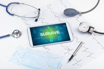 Tablet pc and doctor tools with SURVIVE inscription, coronavirus concept