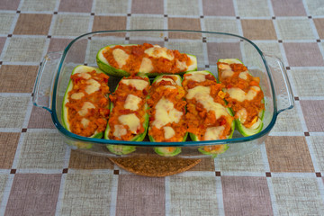Zucchini stuffed with minced meat, cheese and mushrooms. Oven baked. The zucchini are in a glass bowl. On a square tablecloth table.