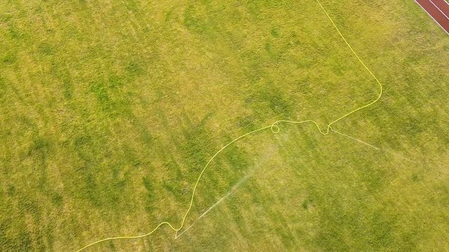 Top down aerial view of football field surface covered with green grass and sprinklers spraying water.