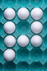 Full colourful teal egg carton box with white chicken eggs forming a 'P' well lit in studio lighting