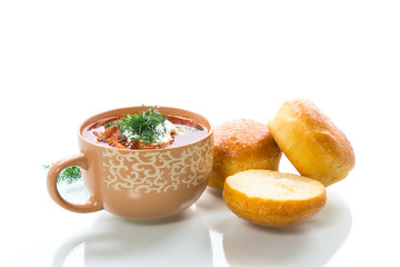hot beetroot soup with sour cream, herbs and rolls in a ceramic bowl