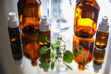 Brown transparent bottles with green sprouts on a mirrored table