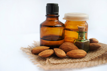 Almond essential oil in a bottle. Selective focus. Three small bottles and a mendal on burlap, white background.