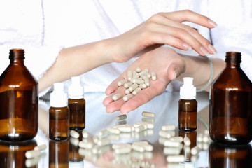 Many pills are in the girl's palm. There are jars of medicine on the table