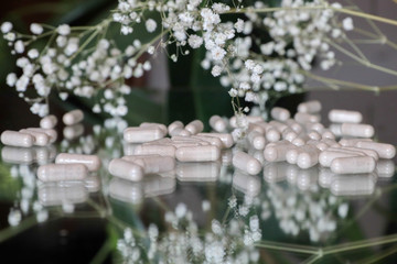Pills on a glass table in flowers and leaves close up
