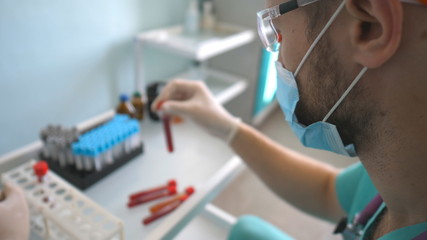 Profile of scientist testing test tube with blood sample to coronavirus. Young laboratory worker in protective glasses examining blood samples to COVID-19. Safety life from pandemic of corona virus