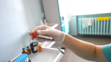 Scientist examining test tube with blood sample to coronavirus. Lab worker with protective gloves testing blood samples to COVID-19. Concept of health and safety life from pandemic of corona virus