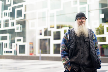 Mature handsome bearded hipster man thinking in the city streets outdoors