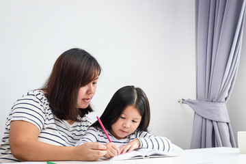 Mothers teach homework to the little daughter on their home desk. Social distance concept for reducing the spread of coronavirus (COVID-19). copy space