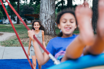 Fototapeta na wymiar Smiling girl pushing sister on swing in park